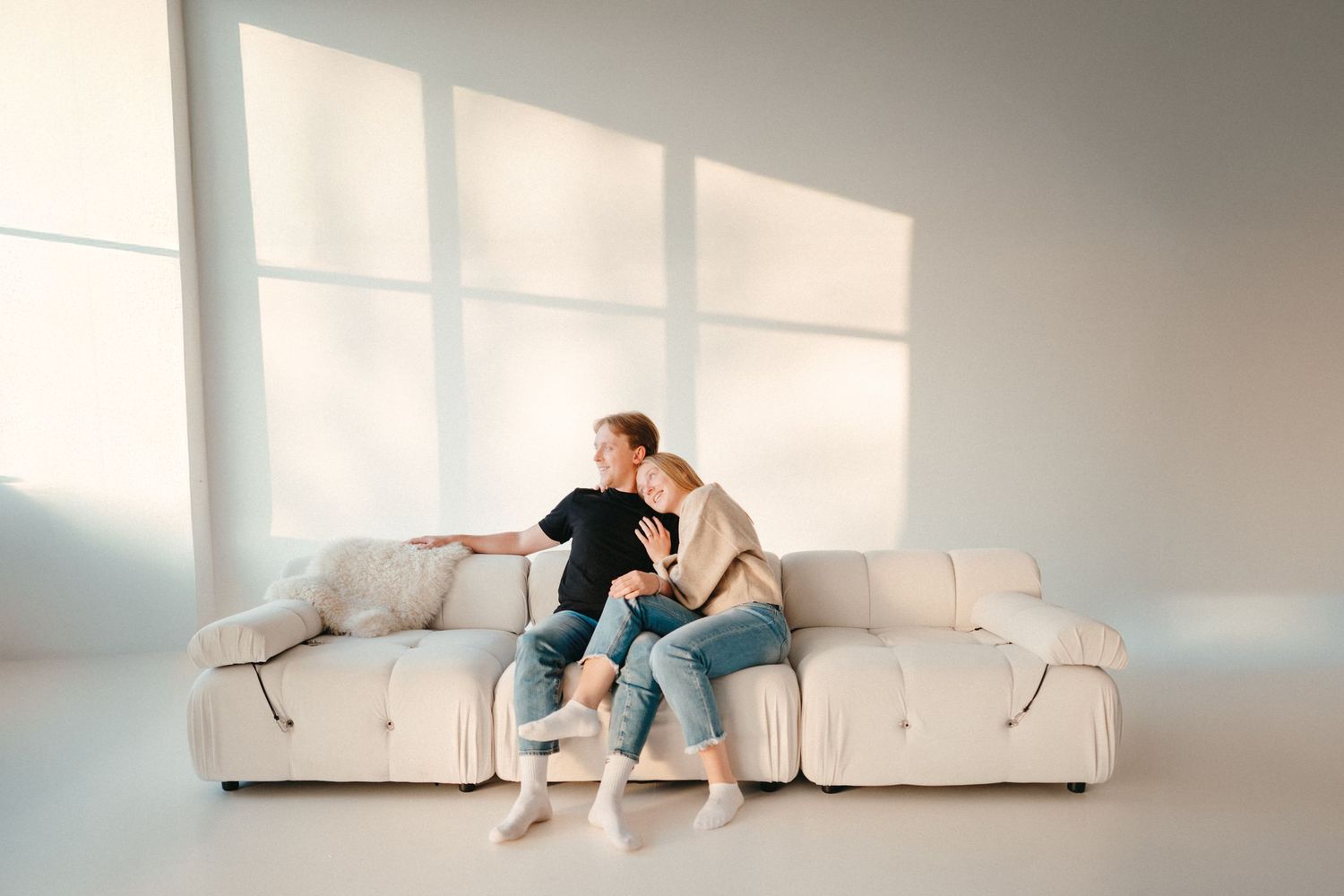 Studio couples portrait with a young couple on a couch, soft natural light, clean neutral tones and a modern intimate feel.