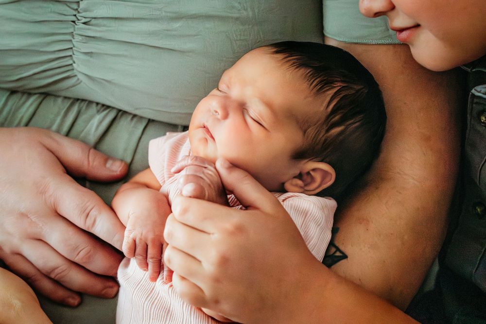 Newborn baby sleeping peacefully in parents arms, wrapped in a soft pink blanket.