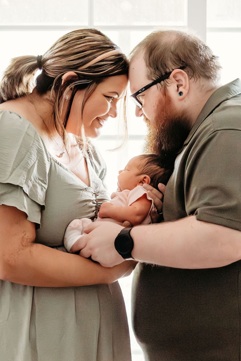 New parents smiling and cradling their newborn baby together in a warm, intimate portrait.