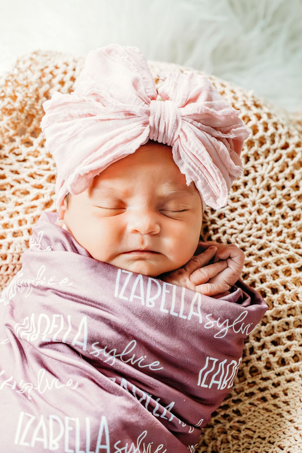 Sleeping newborn baby girl named Izabella swaddled in a purple personalized blanket wearing a pink bow headband.