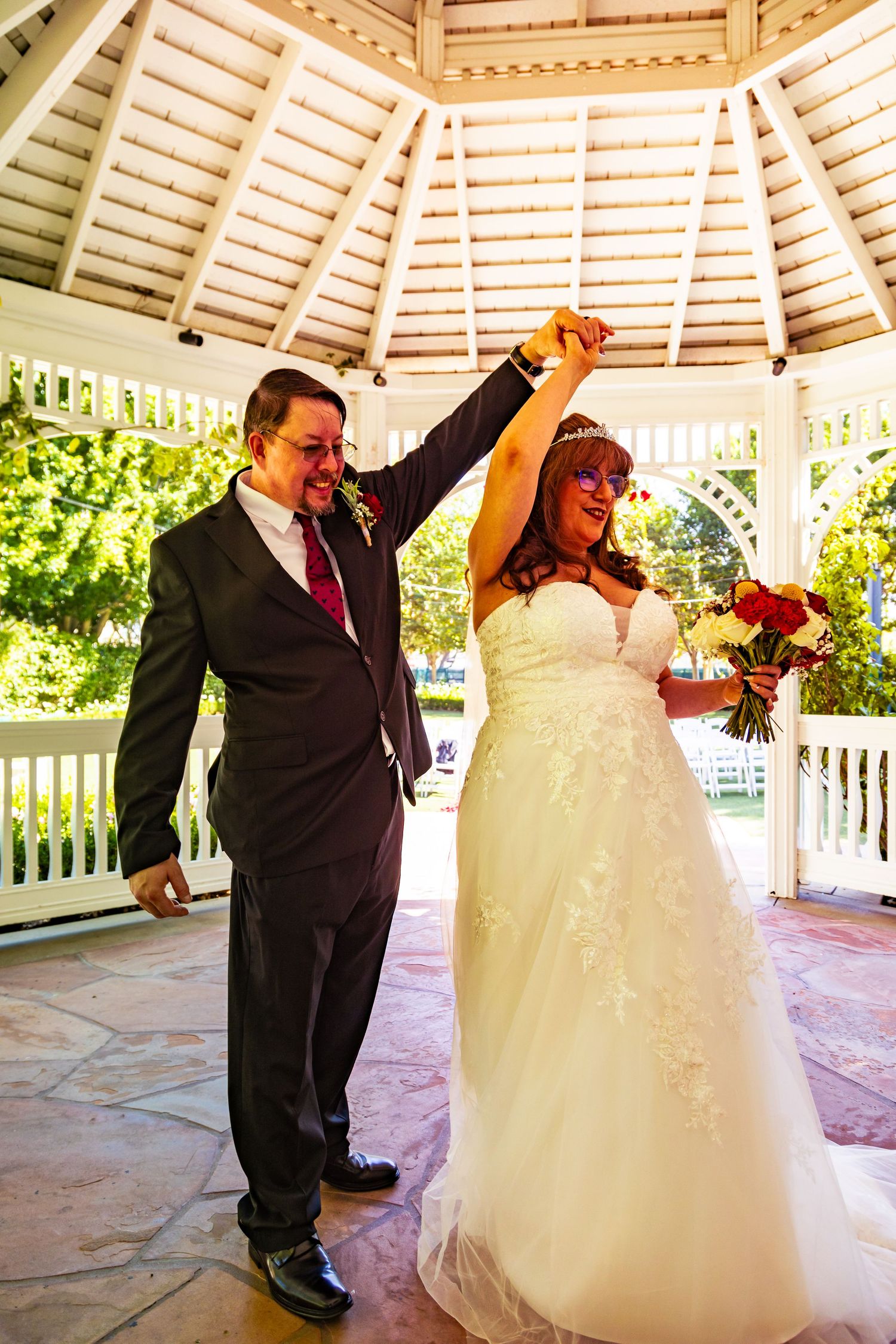 Joyful bride and groom celebrate under a gazebo, raising hands in triumph after their wedding ceremony.