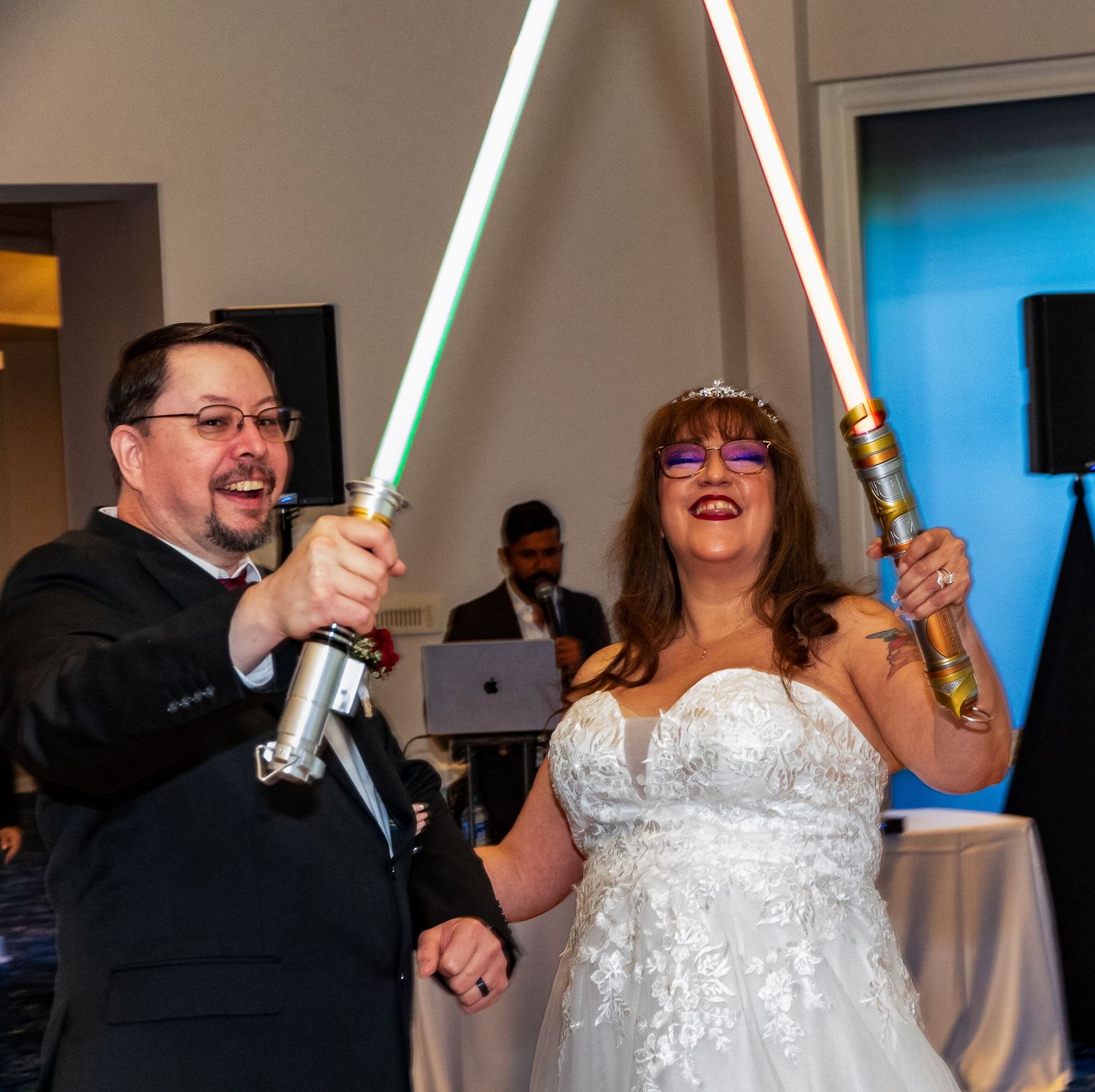Bride and groom joyfully wielding colorful lightsabers at their Star Wars themed wedding reception.