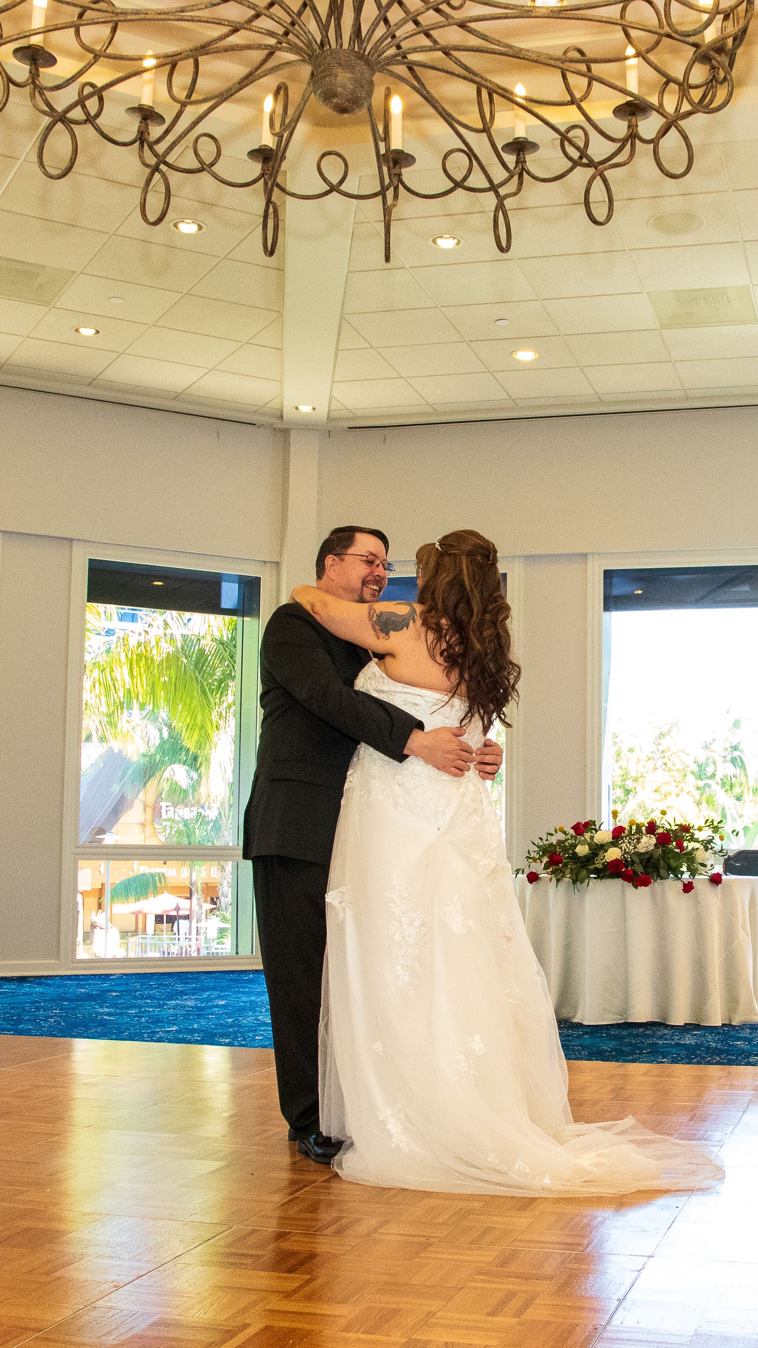 Bride and groom share their first dance in an elegant ballroom with chandelier and floral centerpieces.