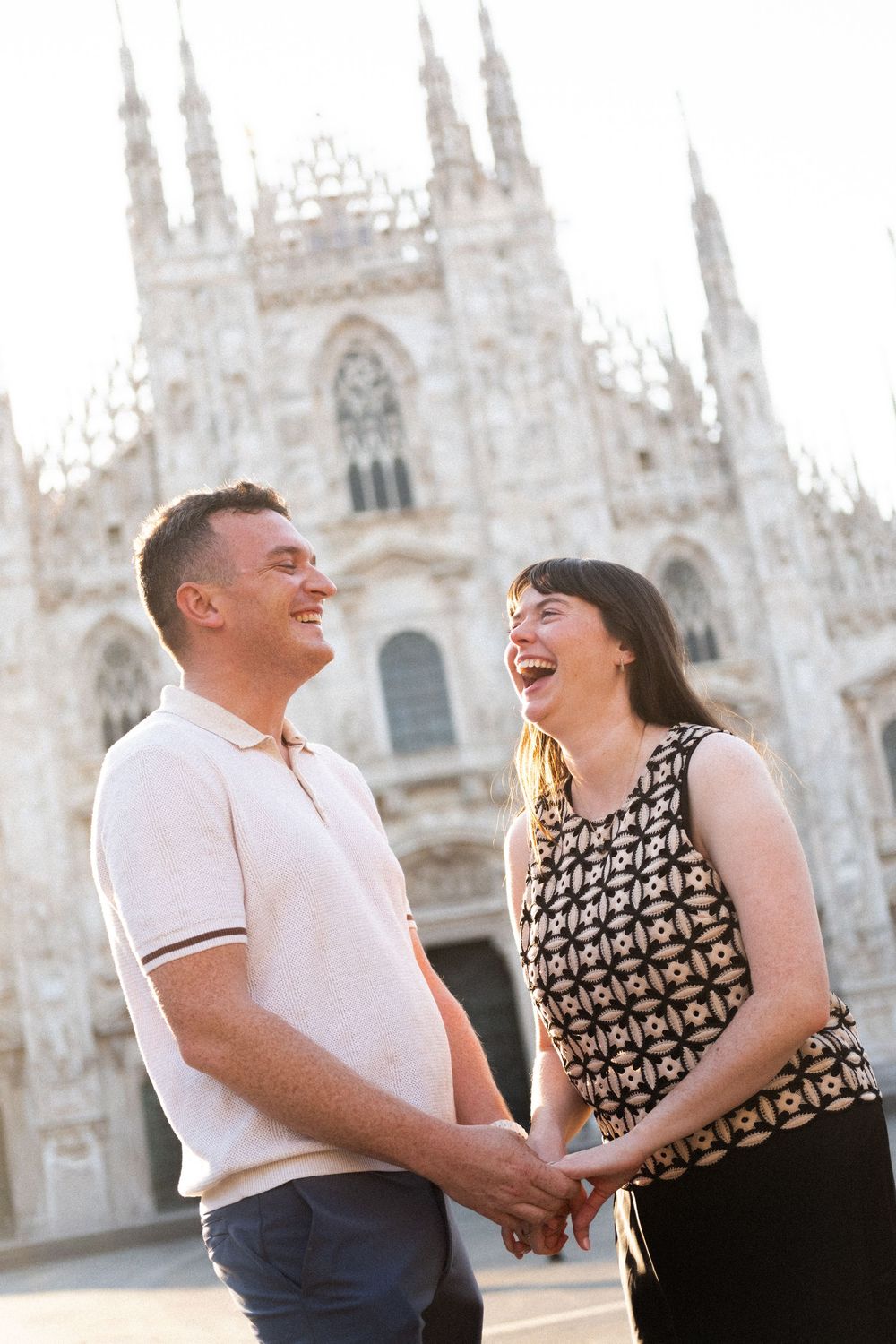 Happy couple holding hands and laughing in front of Milan Cathedral, Duomo di Milano, on a sunny day.