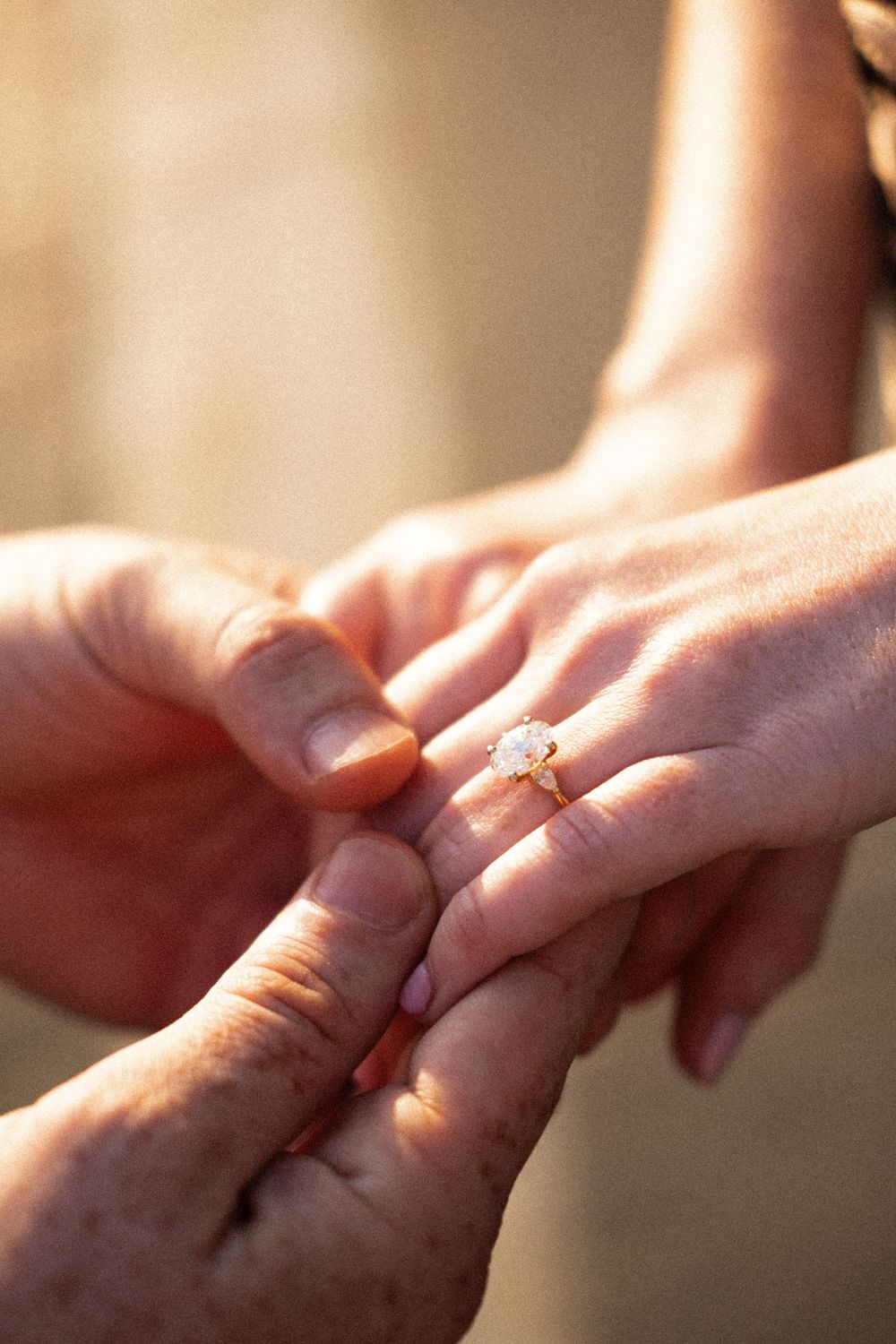 Close-up of a person placing a gold diamond engagement ring on a partner's finger during a proposal.