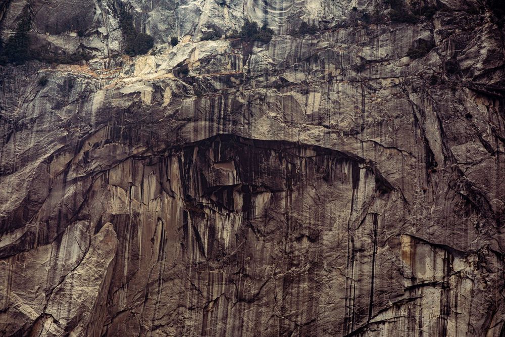 Close-up of a rugged dark rock face with dramatic streaks and natural erosion patterns on a cliff wall.