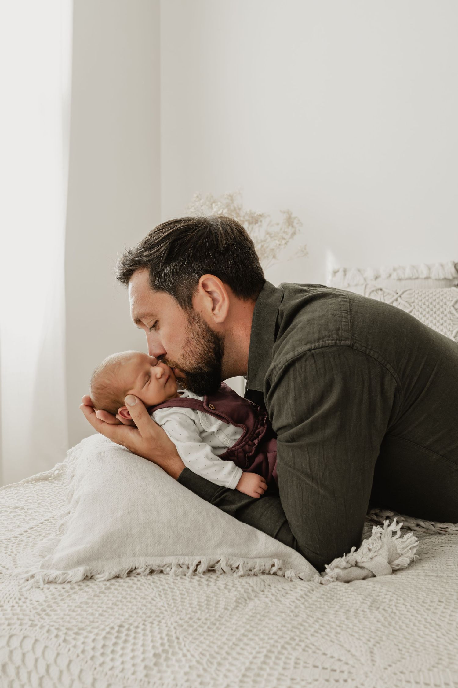 Papa küsst sein Baby beim Newbornfotoshooting in Tulln auf dem Shootingbett im Fotoatelier