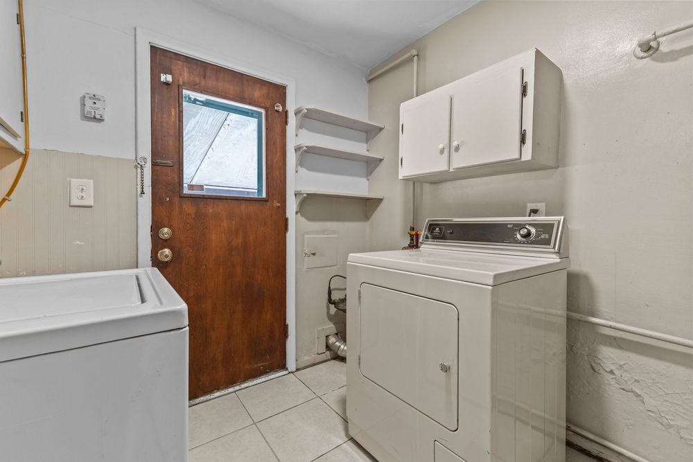 Laundry room with washer and dryer, white cabinets, shelving, and tile floor.