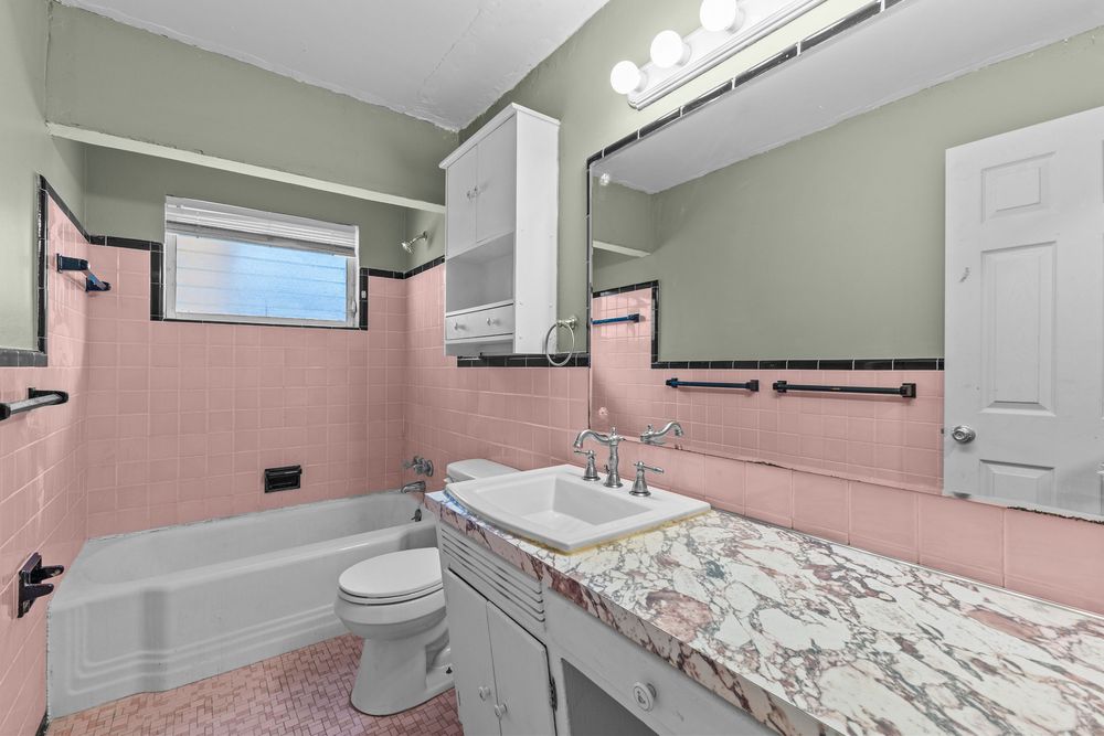 Vintage pink tiled bathroom with tub, toilet, vanity, and marble countertop.