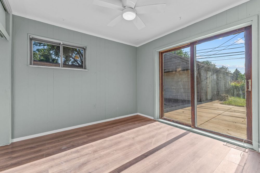 Empty room with hardwood floors, ceiling fan, and sliding glass patio door.