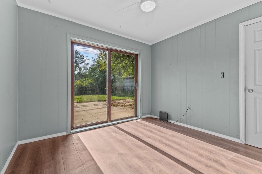 Bright empty room with hardwood floors, sliding glass door, and ceiling fan.