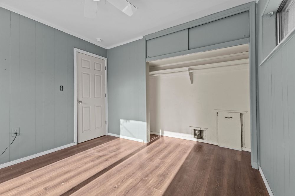 Empty bedroom with hardwood floors, ceiling fan, closet, and wood panel walls.