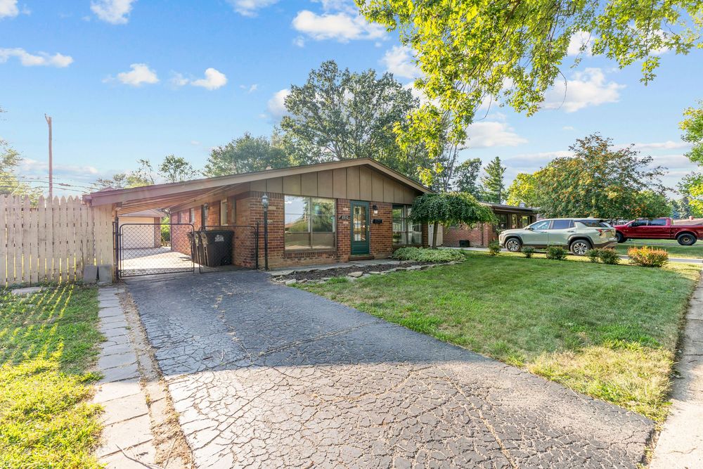 Ranch-style home with brick exterior, carport, driveway, and mature trees.