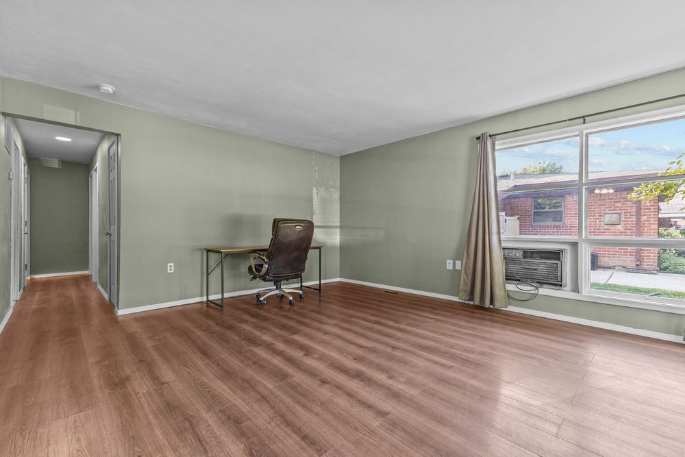 Bright home office with hardwood floors, large window, desk, and neutral sage green walls.