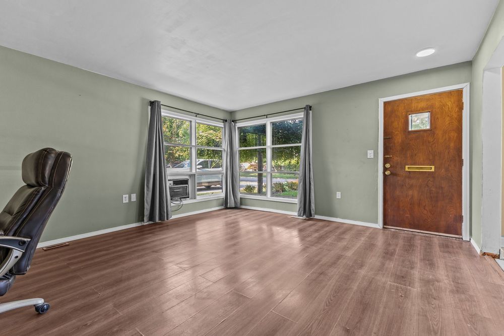 Spacious entryway with hardwood floors, sage green walls, large window, and classic wooden front door.