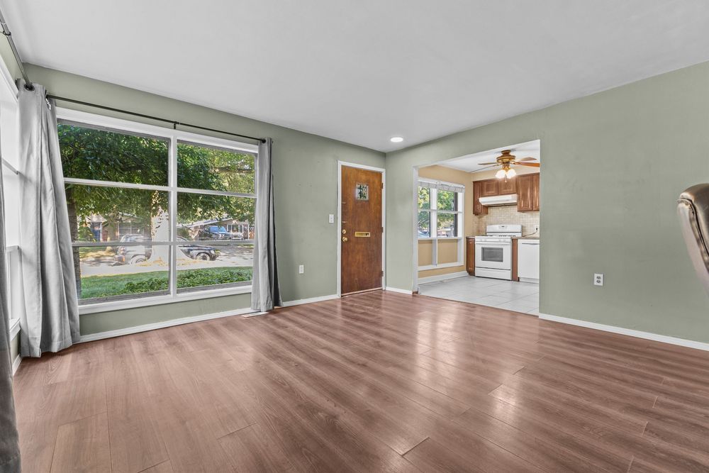 Open living area with hardwood floors, sage green walls, large windows, and view into kitchen beyond.