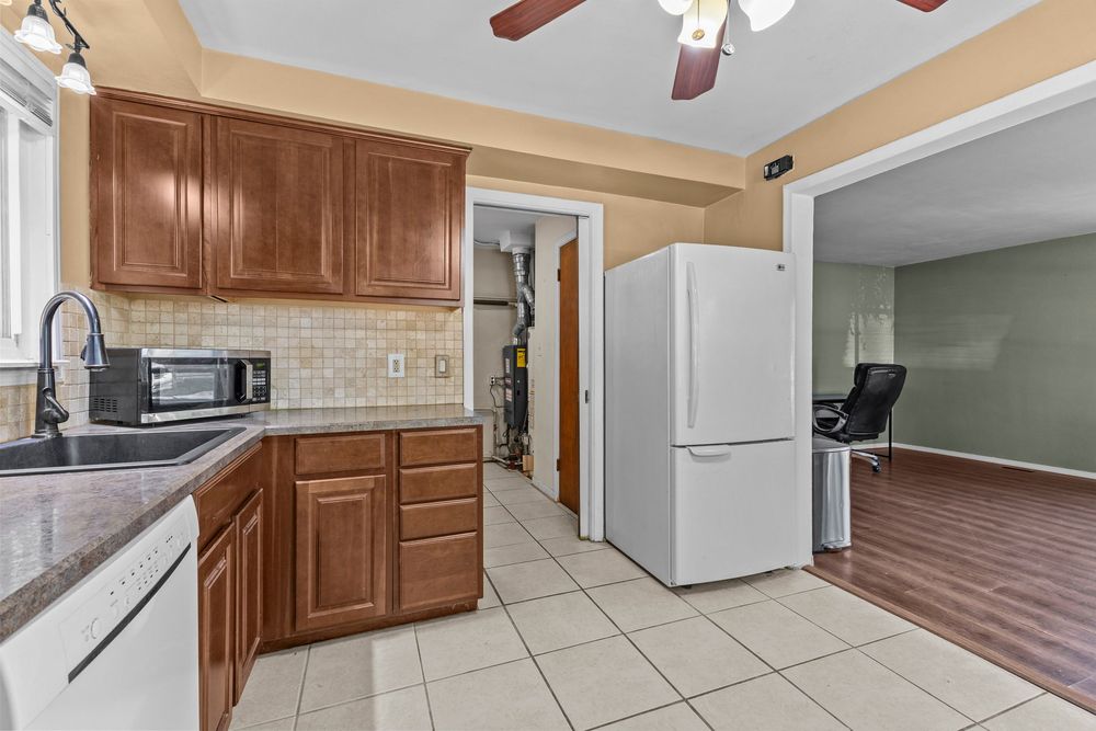 Kitchen with brown cabinets, white appliances, tile backsplash, and tile flooring.