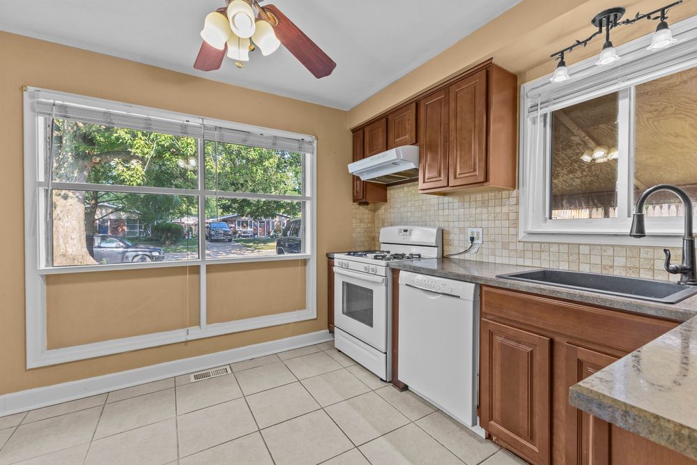 Kitchen featuring brown cabinets, white range, tile backsplash, and large window.