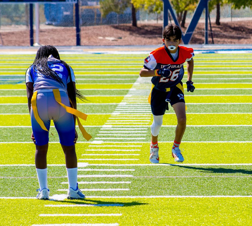 Two female flag football players compete on a bright green turf field during an outdoor game.