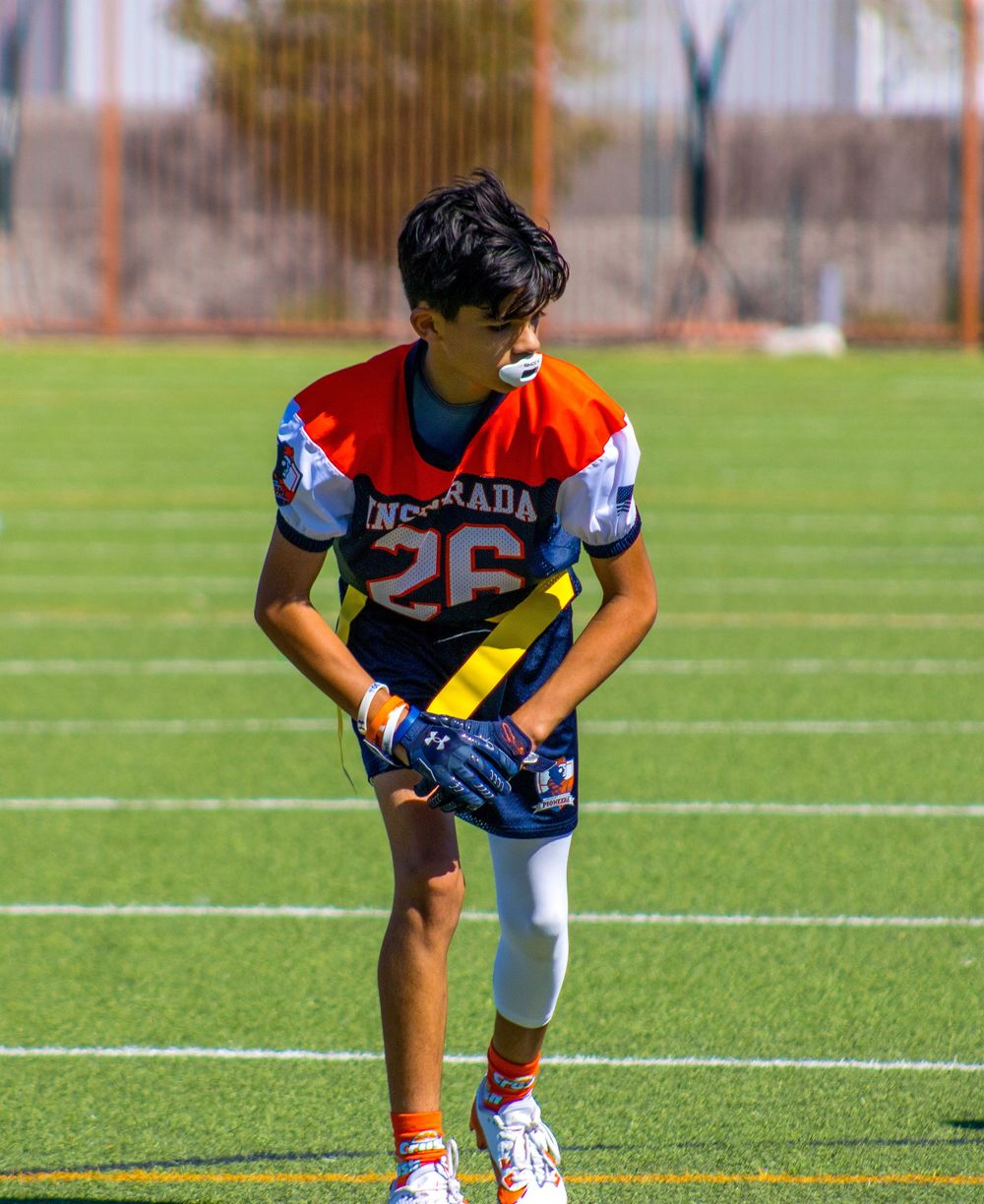 Young football player wearing jersey number 26 stands on a green turf field during a game or practice.