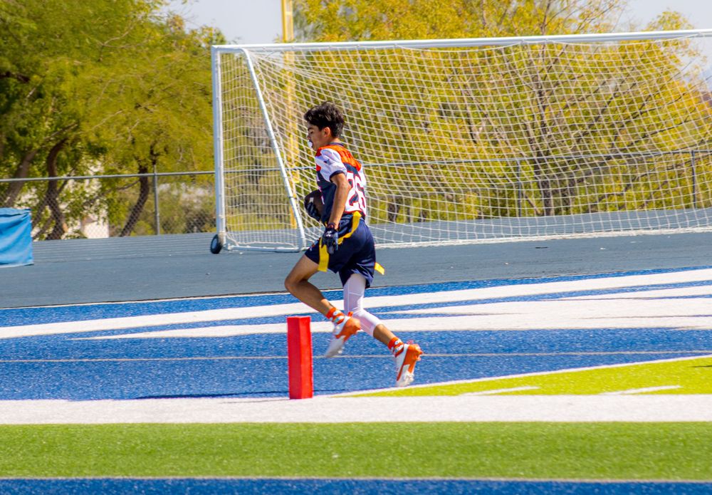 Soccer player running near goal post on blue turf field during outdoor match.