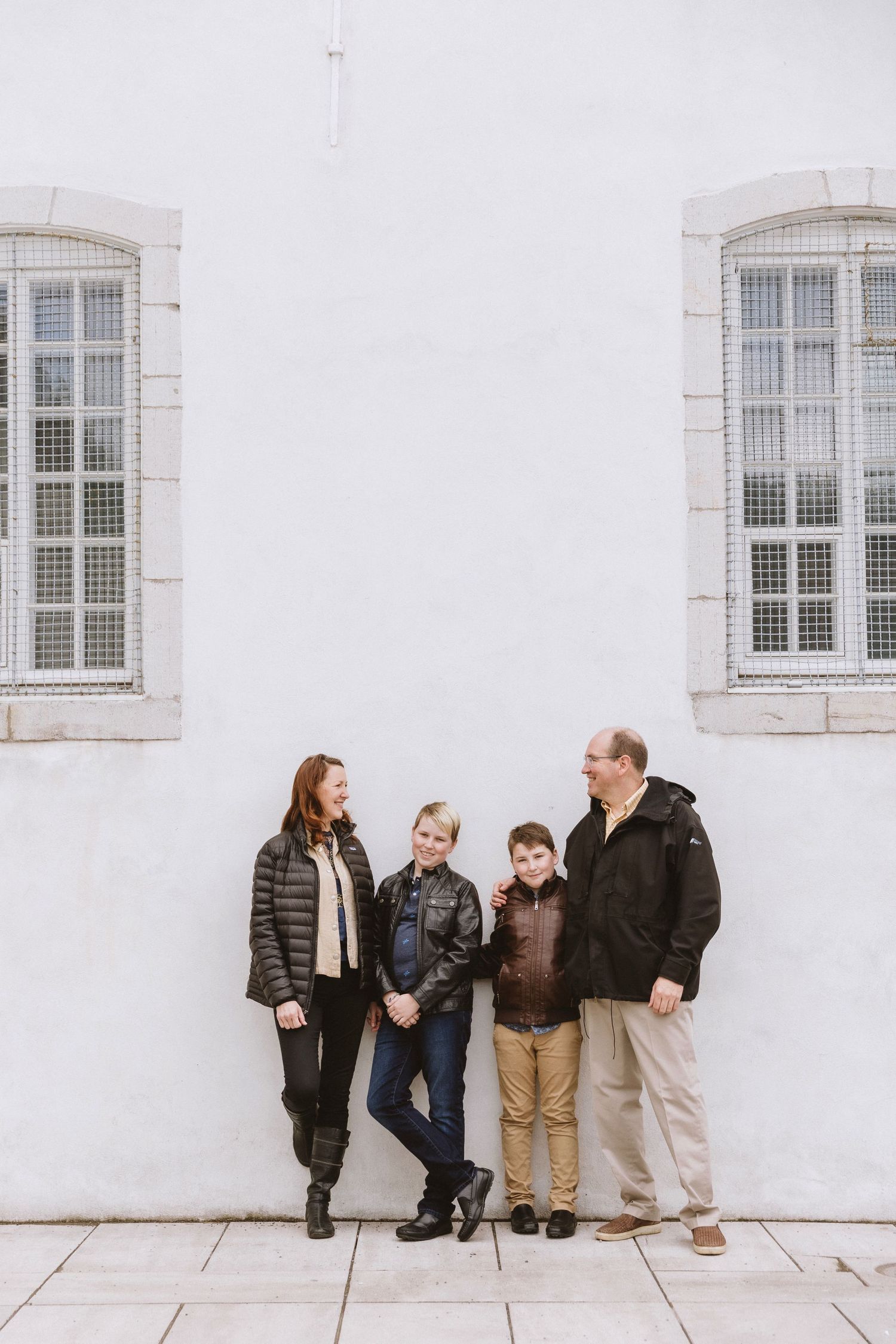 Group posing against white stone wall with vintage windows in Quebec City.