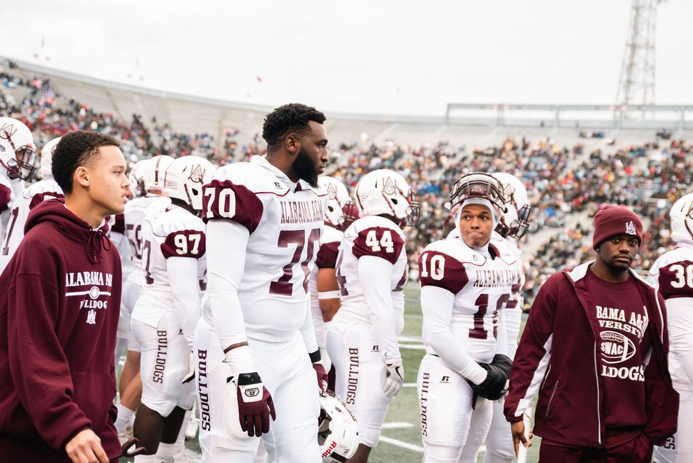 Alabama A&M football players in maroon uniforms walk on the sideline during a college football game.