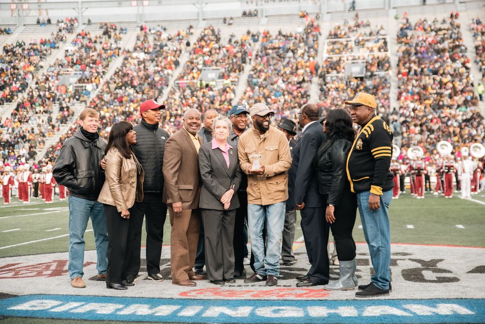 Group of people gathered on a football field at Birmingham stadium during a packed game day ceremony.