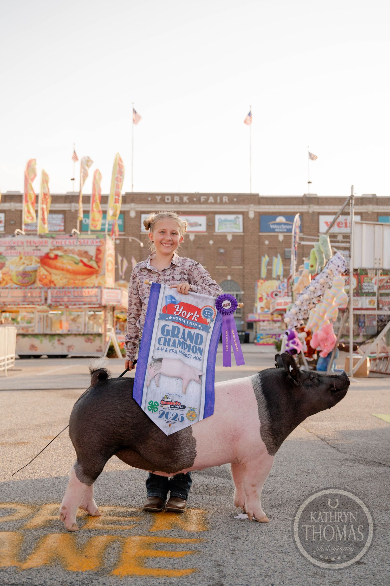 Youth exhibitor proudly displays Grand Champion ribbon with show pig at York Fair 4-H competition.