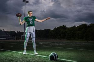 Football player #5 in green jersey poses on field holding ball under dramatic stormy sky.