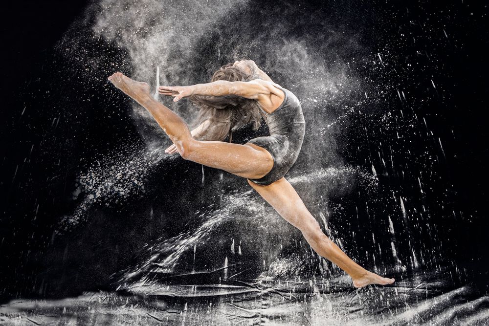 High school senior girl in dancing leap with dramatic lighting throwing flour