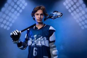 Young lacrosse player in blue jersey number 6 poses with stick under dramatic blue stadium lighting.
