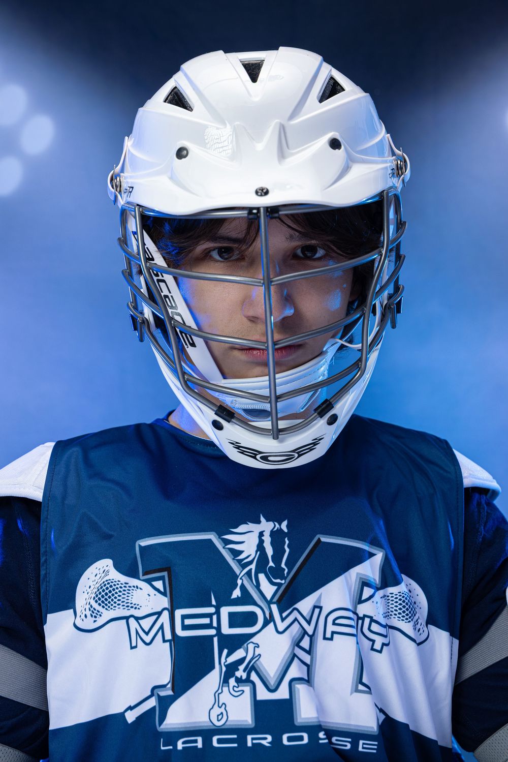 Medway Lacrosse player in white helmet and blue jersey poses dramatically under blue stadium lights.