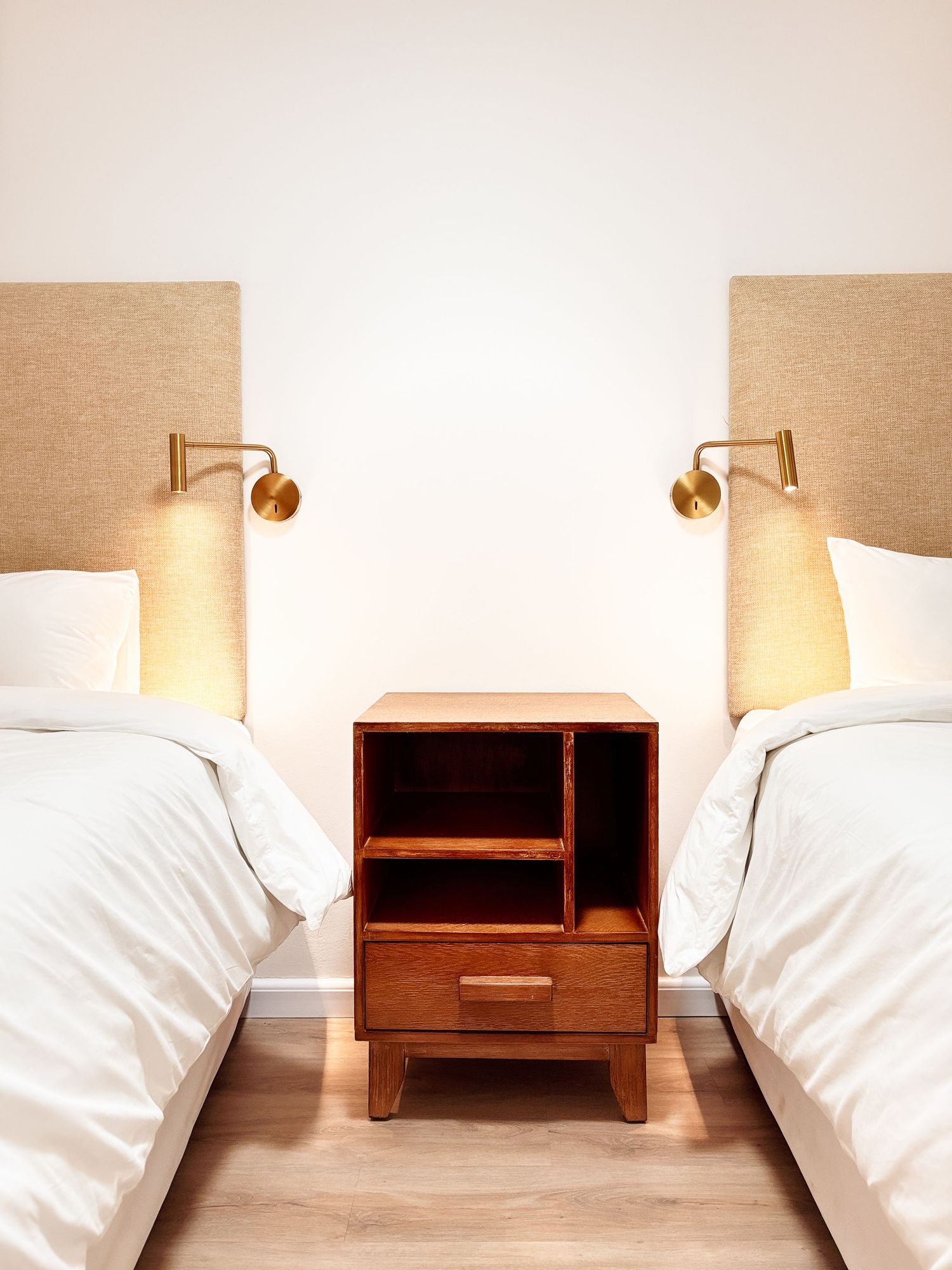 Neatly styled twin bedroom with white linen, wooden bedside table and warm wall sconce lighting — lodge accommodation photography