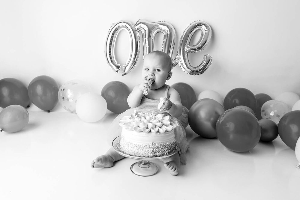 Baby smashing first birthday cake in black and white photo with one balloon.