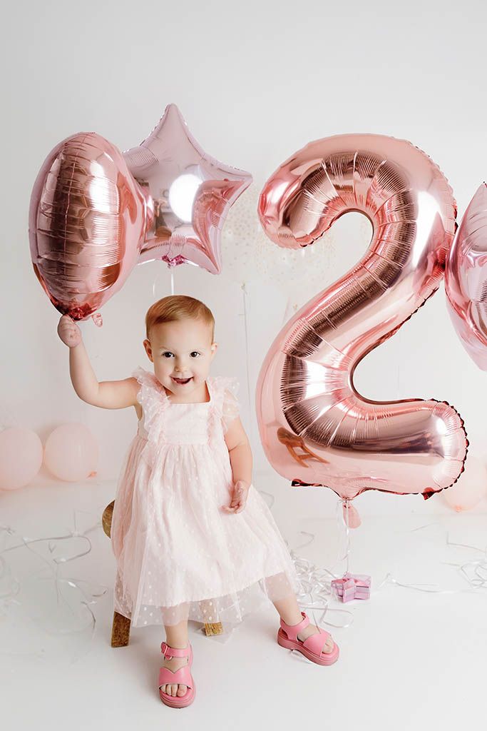 Joyful toddler in pink dress holding rose gold balloons by Temecula child photographer.