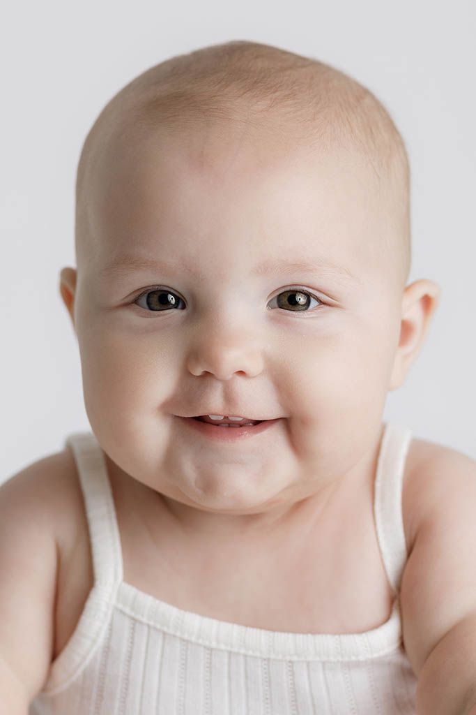 Adorable smiling baby in white tank top with chubby cheeks and bright eyes on white background.
