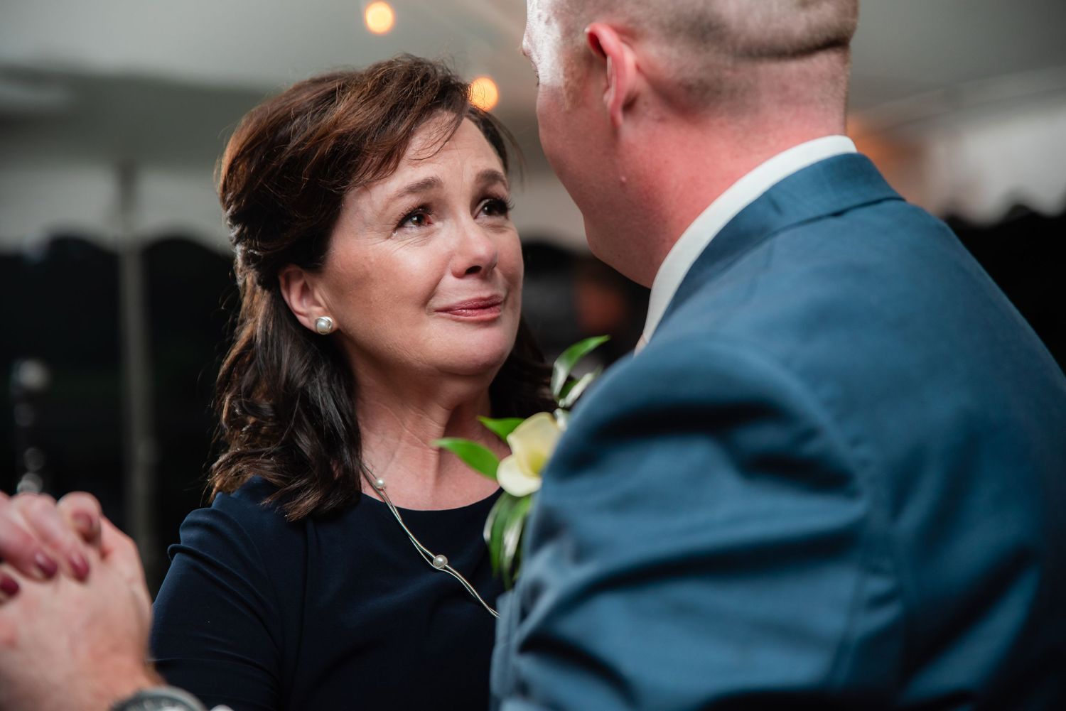 Emotional mother dancing with groom at wedding reception, tears of joy on her face.