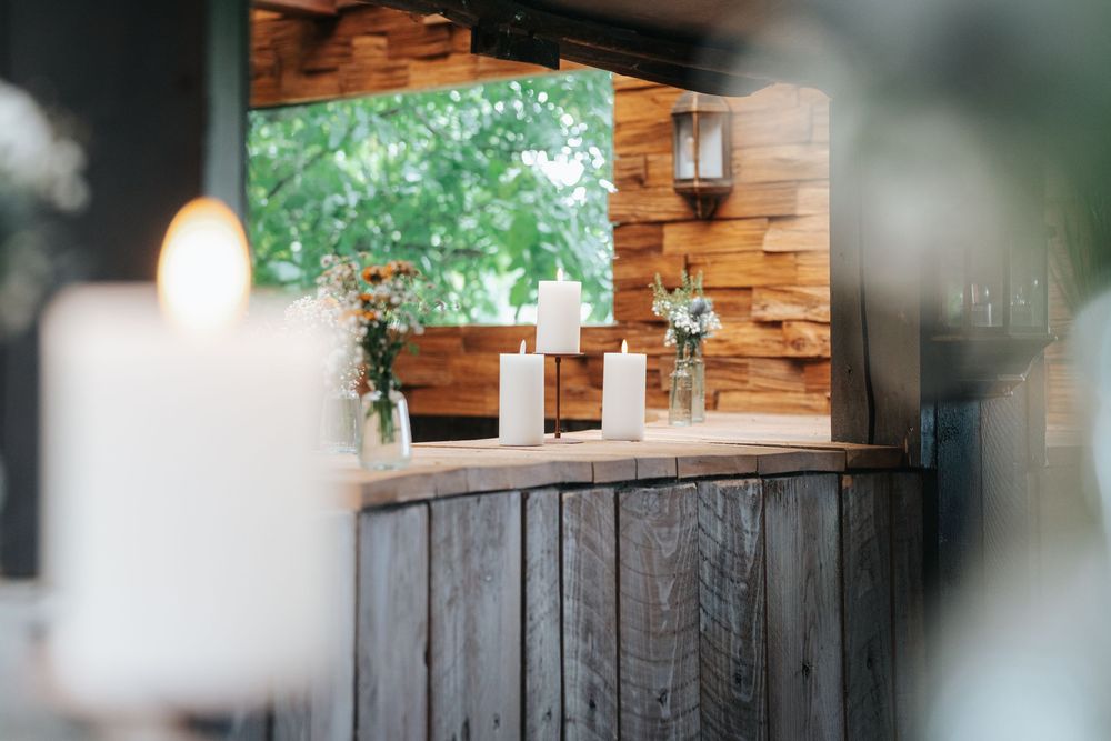 Rustic wooden bar with white candles and floral arrangements in a cozy venue setting.