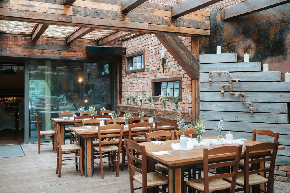 Rustic restaurant dining area with wooden tables, brick walls, and exposed beam ceiling in a cozy indoor setting.
