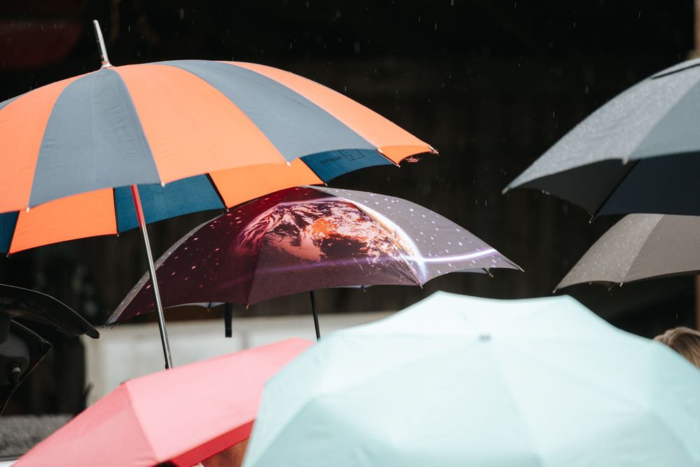 Colorful umbrellas in the rain, including orange, teal, and clear globe-printed umbrella, on a rainy day.