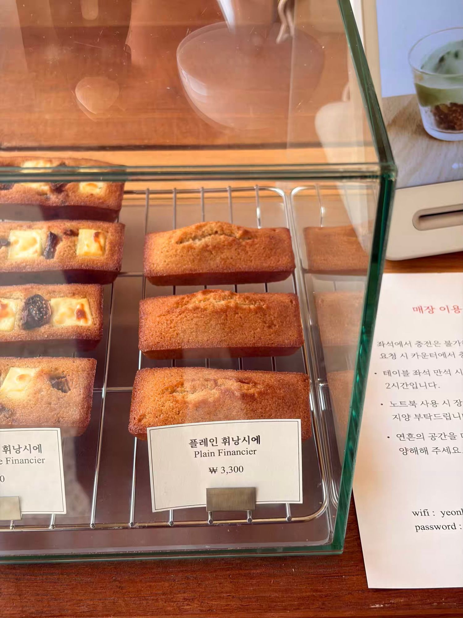 Korean bakery display case with golden plain financier cakes priced at 3,300 won on a wire rack.