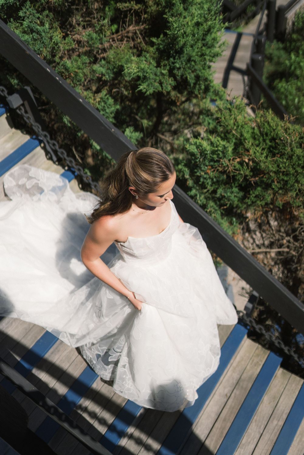 Aerial view of bride in strapless white ball gown descending wooden staircase surrounded by greenery.
