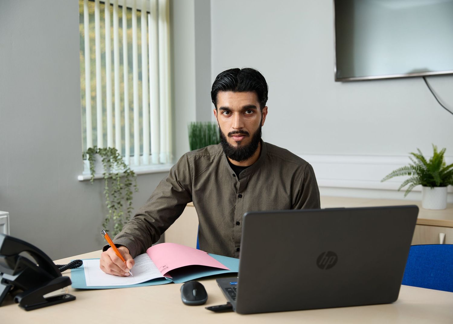 Young man writing notes at desk with HP laptop in modern office setting.
