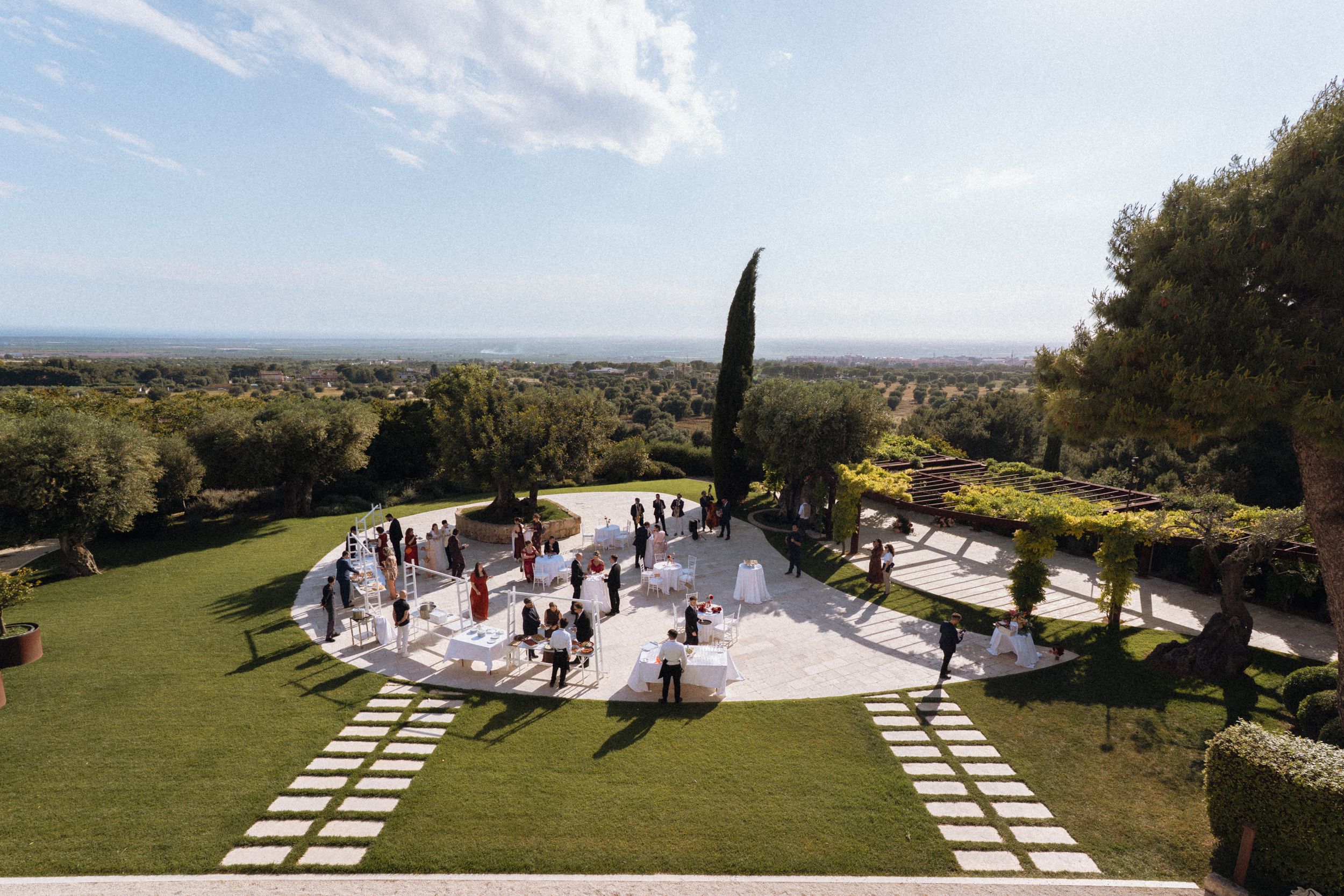Aerial view of an elegant outdoor wedding reception on a terrace surrounded by lush gardens and scenic landscape.