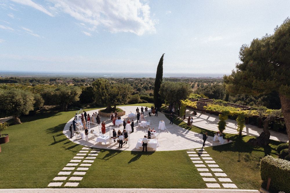 Aerial view of an elegant outdoor wedding reception on a terrace surrounded by lush gardens and scenic landscape.