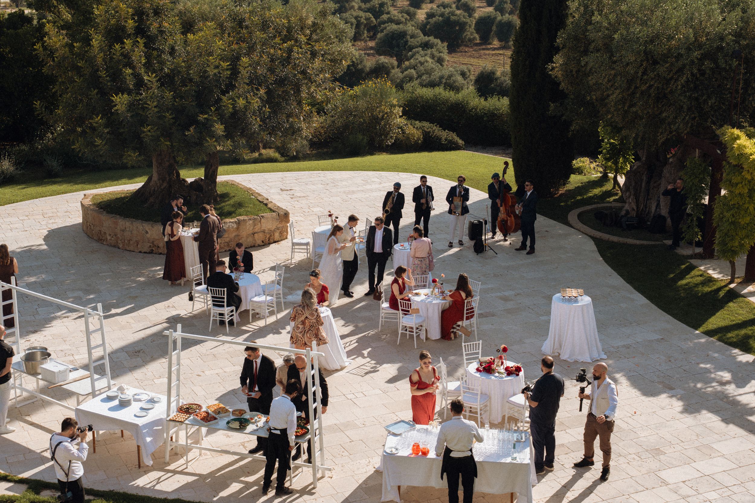 Aerial view of an elegant outdoor wedding reception on a stone terrace surrounded by lush greenery.