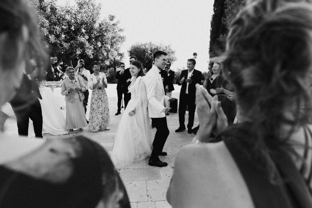 Black and white wedding photo of bride and groom walking through cheering guests outdoors.