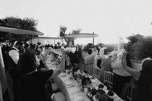 Black and white outdoor wedding reception with guests raising glasses for a toast along elegantly set long tables.