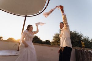 Bride and groom joyfully waving fabric together outdoors at sunset during wedding celebration.
